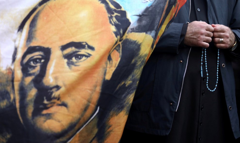 Un sacerdote sostiene un rosario junto a una bandera con el retrato del dictador Francisco Franco afuera del cementerio Mingorrubio-El Pardo. REUTERS / Sergio Perez