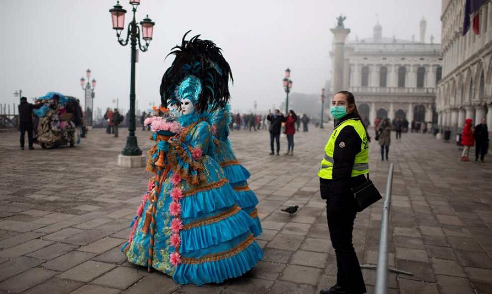 Un guardia de seguridad con una máscara protectora junto a personas disfrazadas paseando por las calles de Venecia cerca de la plaza San Marco. EFE