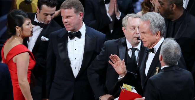 Los socios PricewaterhouseCoopers (PwC), Martha Ruiz y Brian Cullinan (a la izquierda de la imagen), conversan en el escenario de la gala de los Premios Oscar de Hollywood, mientras un regidor conversa con el actor Warren Beatty, quien sostiene uno de los