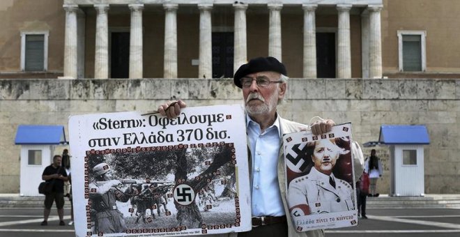 Un hombre sostiene un cartel de la canciller Angela Merkel como si fuera un miembro del partido nazi frente al Parlamento griego en la marcha por el Día de los Trabajadores en Atenas. /EFE