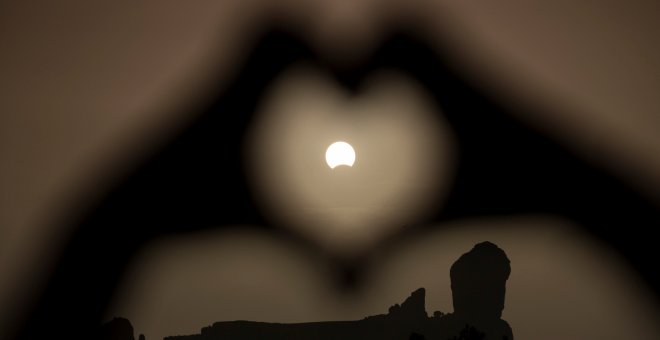 Una mujer hace el gesto del corazón con las manos enmarcando el eclipse de Sol, en el Roque Nublo, en Gran Canaria. REUTERS/Borja Suarez