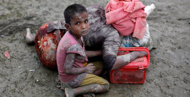 Una niña ronhinyá sentada junto a su madre, que descansa tras cruzar la frontera entre Brimania y Bangladesh. - REUTERS