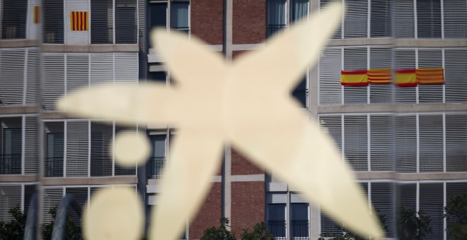 El logo de Caixabank, en su sede de Barcelona, donde se reflejan los edificios vecinos con banderas españolas y catalanas. REUTERS/Albert Gea