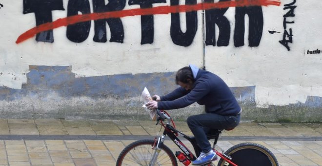 Un hombre pasea en bicicleta por un graffiti contra la tortura en el pueblo vasco de Agurain / Salvatierra. ANDER GILLENEA / AFP