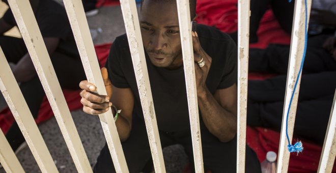 Un joven de senegal llama por teléfono en el muelle del puerto de Algeciras, donde ha pasado dos noches por falta de espacio en dependencias policiales y polideportivos. JAIRO VARGAS