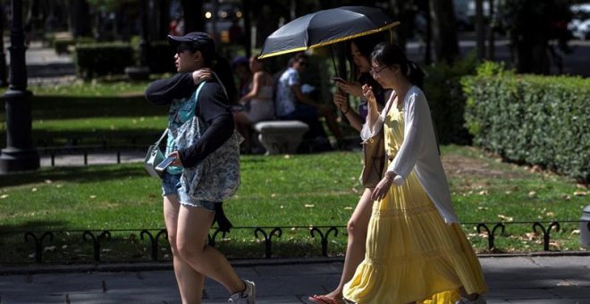 Varios turistas se protegen del sol durante la ola de calor en el madrileño parque de El Retiro. / EFE