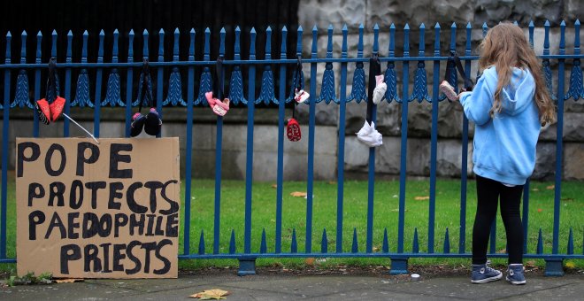 Una niña de espaldas junto a pancarta en la que dice que ""El Papa protege a los curas pederastas" en Dublín. /REUTERS