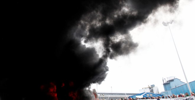 Trabajadores de la planta Alcoa de A Coruña, durante la concentración que llevan a cabo a las puertas de la fábrica, donde han quemado neumáticos y cortado el tráfico, en protesta y en lucha contra el cierre de la aluminera, que supondría el despido colec