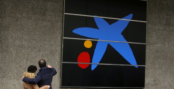 Una pareja se hace un selfi junto al logo de Caixabank en su sede en Madrid. REUTERS/Sergio Perez