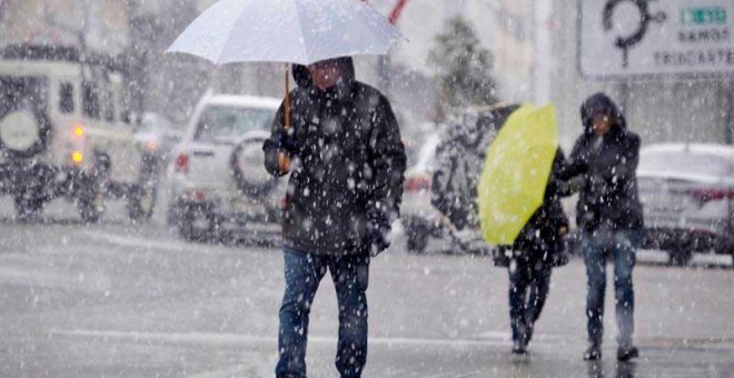 Varias personas caminan bajo una intensa nevada, en la localidad lucense de Piedrafita do Cebreiro ayer lunes. (ELISEO TRIGO | EFE)