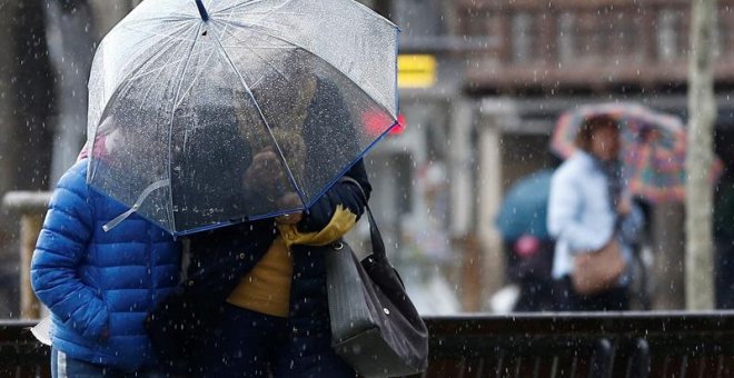 Dos personas se protegen del viento y de la lluvia este jueves en la Plaza del Castillo de Pamplona. / Jesús Diges (EFE)