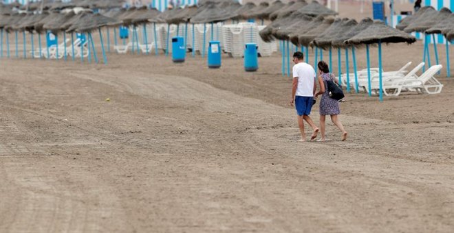 Una pareja pasea por la playa de la Malvarrosa en la que la afluencia de gente ha descendido notablemente debido en gran medida al descenso de temperaturas, a los chubascos y al cielo nublado. /EFE