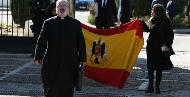 24/10/2019.- El sacerdote Ramón Tejero, que ha oficiado la misa de la reinhumación de Francisco Franco, a su salida del cementerio de Mingorrubio junto a dos familiares del dictador que portan una bandera española con el escudo franquista, tras enterrar a