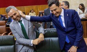 El presidente andaluz, Juanma Moreno, bromea con el consejero de Hacienda, Juan Bravo, al inicio del pleno del Parlamento de Andalucía. /EFE