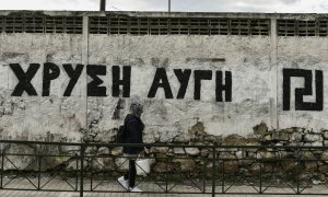 Una mujer pasa junto a una pared pintada con el logotipo del partido neonazi griego Amanecer Dorado, en Atenas. AFP/Aris Messinis