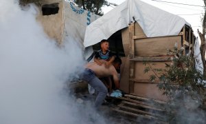 Un solicitante de asilo carga con su hijo para alejarlo de los gases lacrimógenos lanzados por la policía para sofocar las protestas de los refugiados el pasado domingo en el campo de refugiados de Moria, en la isla de Lesbos, Grecia.-REUTERS