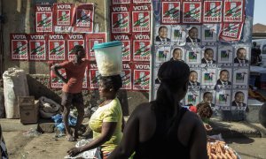 Vendedores y clientes caminan por un muro cubierto con carteles de la campaña de las elecciones presidenciales de Mozambique en el mercado Xipamanine en Maputo. - AFP