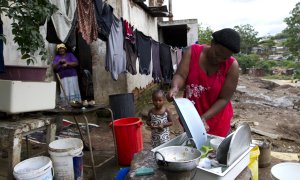 Una mujer lava los platos junto a su hijo en Durban. REUTERS