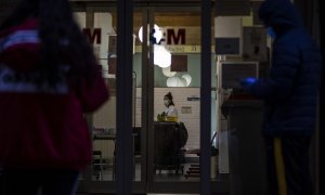 Las puertas de un hospital madrileño muestran personas esperando con mascarillas y guantes y una trabajadora sanitaria. / JAIRO VARGAS