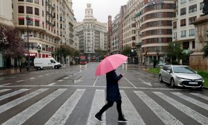 Un hombre protegido con paraguas en la plaza del Ayuntamiento de Valencia prácticamente vacía durante el decimoséptimo día del estado de alarma decretado por el Gobierno. EFE/Kai Försterling