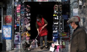 Una mujer con mascarilla limpia la entrada de su tienda en Pekín.. REUTERS/Carlos Garcia Rawlins