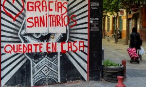 Una mujer con un carro de la compra pasa junto a un comercio cerrado con una pintada de agradecimiento a los sanitarios en una céntrica calle de Sevilla, hoy miércoles en la séptima semana de confinamiento decretado en el Estado de Alarma debido a la cris