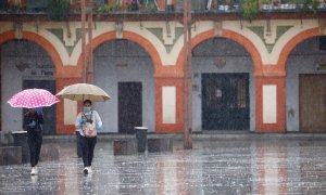 Dos mujeres con mascarillas y paraguas caminan por Córdoba. EFE/Salas