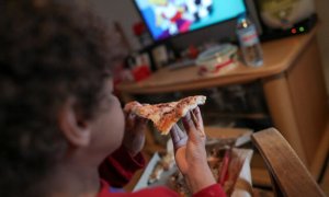 Un niño come un trozo de pizza del menú infantil de Telepizza mientras ve la televisión en su casa. EUROPA PRESS / JESÚS HELLÍN