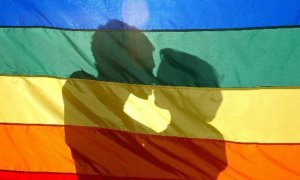 Una pareja se besa tras la bandera del arcoíris, símbolo del movimiento LGTBI.