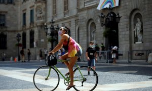 Una joven pasea con su bicleta , protegida con su mascarilla, este jueves, primer día en que es obligatorio el uso de mascarillas en toda Cataluña aunque se puedan guardar las distancias.EFE/Toni Albir