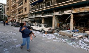 Una mujer lleva a un niño mientras pasa por las tiendas dañadas tras la explosión del martes en Beirut, Líbano