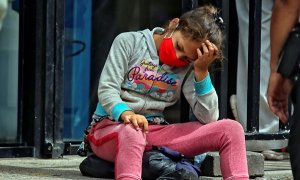 Una niña descansa en unas gradas mientras sus padres hacen fila para comprar alimentos. EFE/Gustavo Amador