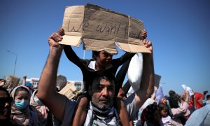 Un hombre sujeta a un niño durante las protestas pidiendo soluciones tras el incendio del campo de refugiados en Moria, Lesbos. / REUTERS