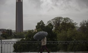 Un hombre protegido con un paraguas camina por el puente de Triana durante la alerta amarilla por tormentas en Sevilla. María José López / Europa Press / Archivo