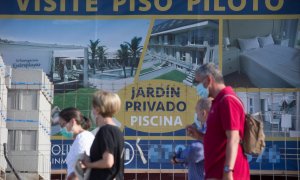 Varias personas caminan junto a un cartel de viviendas en venta en A Mariña (Lugo/Galicia). Carlos Castro / Europa Press / Archivo