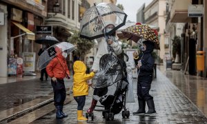 Una mujer con tres menores se protegen de la lluvia con paraguas y chubasqueros en una céntrica calle de València.