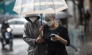 Dos personas se protegen de la lluvia bajo un paraguas, en Sevilla.