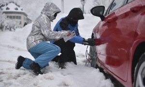 Dos personas ponen las cadenas a las ruedas de su coche por la nieve