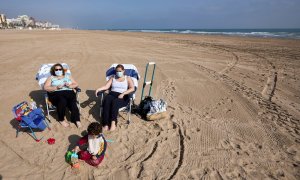 Varias personas toman el sol con mascarilla en la playa de Gandía.