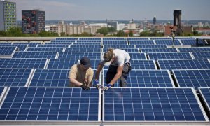 Dos operarios instalan paneles solares en el tejado de un edificios.