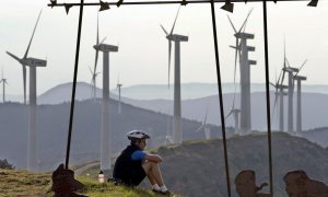 Un ciclista descansa en la Sierra del Perdón, Pamplona, con un paisaje dominado por aerogeneradores eólicos.