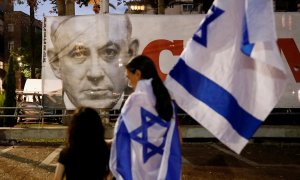 Personas con banderas de Israel pasan por delante de un cartel con la imagen de Benjamin Netanyahu en Tel Aviv, después de la votación en el Parlamento a un nuevo Gobierno de coalición, que pone fin a sus 12 años en el poder. REUTERS/Corinna Kern