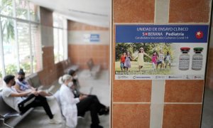 Imagen de archivo de varias personas sentadas cerca de un cartel que anuncia los ensayos clínicos de la vacuna Soberana 02, en una clínica sanitaria en La Habana. - REUTERS