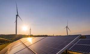 Un parque de energía fotovoltaica, con aerogeneradores de energía eólica al fondo.