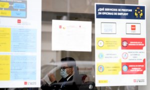 Un hombre con mascarilla tras el cristal de la puerta de una oficina de empleo, SEPE.