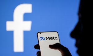 Una mujer sostiene un teléfono inteligente con el logotipo de Meta delante de la imagen de Facebook, a 28 de octubre de 2021.