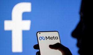 Una mujer sostiene un teléfono inteligente con el logotipo de Meta delante de la imagen de Facebook, a 28 de octubre de 2021.