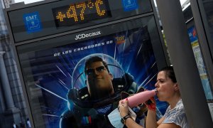 Una mujer bebe agua en la sombra de una parada de autobús de Madrid cuyo termómetro marca 47ºC.