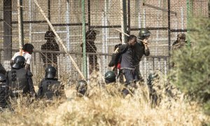 Un miembro de las fuerzas de seguridad marroquíes conduce desde suelo español a uno de los migrantes que logró saltar la valla de Melilla el pasado viernes.