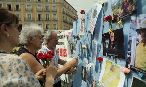 (22/5/22) Varias personas colocan claveles en un mural con retratos de colaboradores en la búsqueda de víctimas por el robo de bebés en España, a 22 de mayo de 2022.